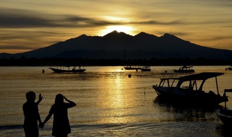 Sepasang wisatawan memperhatikan siluet Gunung Rinjani saat Sunrise (matahari terbit) di pinggiran pantai Gili Trawangan, Desa Gili Indah, Kecamatan Pemenang, Tanjung, Lombok Utara, NTB, Jumat (24/2). 