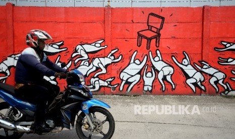 Sepeda motor melintas di sekitar mural yang mengambarkan tentang kursi kekuasaan di Jakarta, Jumat (24/3).