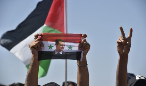 Seseorang memegang bendera Suriah dengan foto Presiden Bashar Assad ketika para pemuda Arab yang berpartisipasi dalam perkemahan musim panas di Lebanon selatan mengikuti tur yang diselenggarakan oleh Hizbullah ke desa perbatasan Shebaa, Lebanon, 05 September 2022. Pemerintah Suriah Bashar Assad memberikan amnesti pada orang-orang yang menghindari wajib militer.