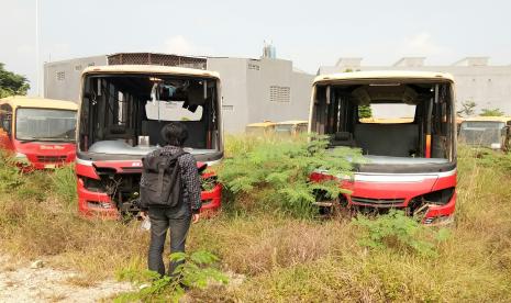 Seseorang mengawasi bangkai bus Transjakarta berwarna oranye di lahan kosong di Jalan Raya Dramaga KM 7, Kabupaten Bogor, Jawa Barat.