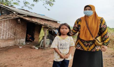 Sinta Murni didampingi petugas berdiri di depan rumahnya di Desa/Kecamatan Kroya, Kabupaten Indramayu, Rabu (23/6). Dalam usianya yang diperkirakan baru tujuh tahun, bocah itu seorang diri mengurus ibunya yang mengalami kondisi agak depresi.