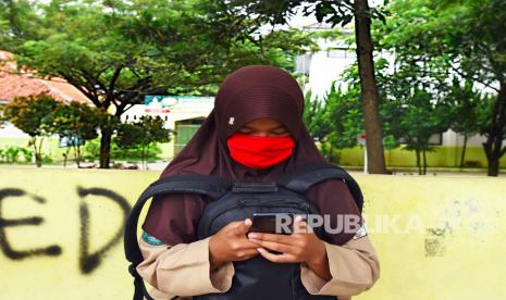 Siswa berseragam Pramuka duduk memainkan ponsel. Pelajar kerap bermain ponsel di sekolah, Heru Budi sebut ini tantangan luar biasa.