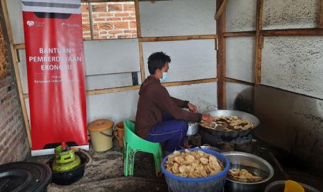 Sumarmi sedang menata kripik tempe sagu hasil irisan bahan yang sudah matang di baki untuk diserahkan ke putranya yang sedang menggoreng. 