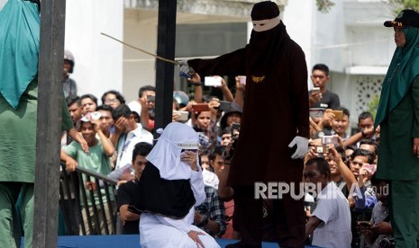 Terpidana (duduk) pelanggar peraturan daerah (qanun) tentang syariat islam menjalani eksekusi hukuman cambuk di hadapan warga di halaman Masjid Jami' Kemukiman Lueng Bata, Banda Aceh, Aceh, Jumat (20/4). 