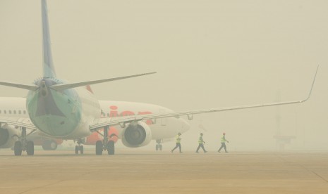 Tiga kru bandara melewati dua pesawat di landasan Bandara Supadio yang diselimuti kabut asap, di landasan Bandara Supadio, Kubu Raya, Kalbar, Rabu (21/10). 