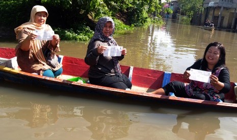 Tiga orang warga menunjukkan formulir hak pilih Pilkada Kabupaten Bandung saat akan menuju TPS dengan menggunakan perahu karena banjir di Kampung Cieunteung, Baleendah, Kabupaten Bandung, Jawa Barat, Rabu (9/12). 