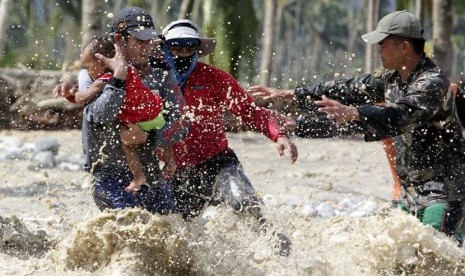 Tim penyelamat mengevakuasi seorang anak yang selamat  bersama ibunya yang tengah hamil menyeberangi sungai di kota New Bataan,Filipina, Kamis (6/12). (Reuters/Erik De Castro)