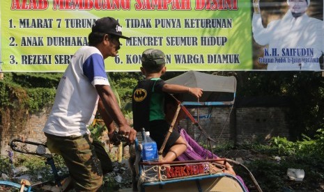 Tukang becak melintas di depan spanduk larangan buang sampah sembarangan (ilustrasi)