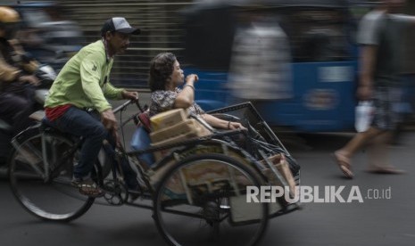 Tukang becak mengangkut penumpang saat melintas di kawasan Petak Sembilan, Glodok, Jakarta, Selasa (16/1).