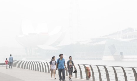 Turis berjalan di area Marina Bay Sands, Singapura, yang tertutup kabut asap akibat kebakaran hutan di Indonesia (23/10).