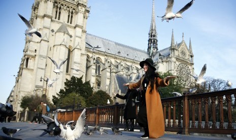 Turis berpose dengan latar Notre Dame de Paris.