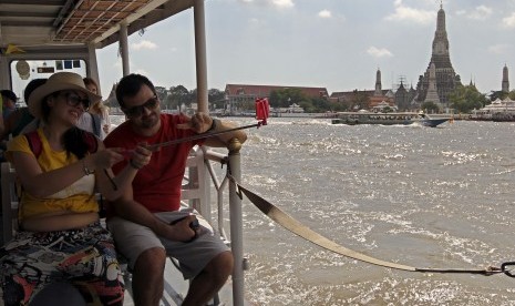 Turis berpose dengan latar Wat Arun di Bangkok.