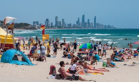 Turis bersantai di pantai berpasir putih dengan pemandangan bangunan pencakar langit Gold Coast, Australia.