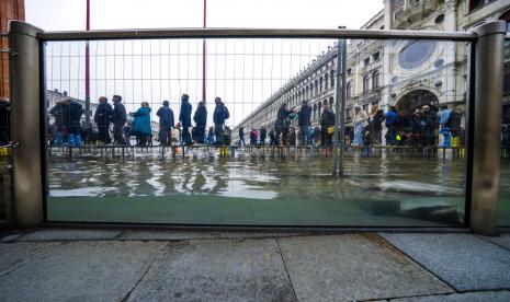 Turis dan penduduk berjalan di catwalk selama gelombang laut sekitar 97 sentimeter (38,18 inci) untuk menyeberangi Alun-alun St. Mark yang banjir di Venesia, Italia utara, Sabtu, 10 Desember 2022, di mana penghalang kaca yang baru dipasang mencegah air laut membanjiri Basilika St Mark yang ikonik berusia 900 tahun. Alun-alun St. Mark adalah area kota dengan lapisan terendah dan sering berakhir di bawah air selama cuaca ekstrem.