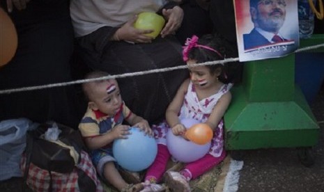 Two Egyptian children play with balloons as they sit next to a picture of Mursi outside Rabaah al-Adawiya mosque, where supporter of Egypt's ousted President Mohammed Mursi have installed a camp and held daily rallies at Nasr City, Cairo, Egypt, Tuesday, A