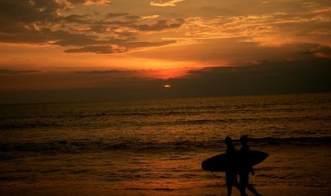 Two surferers pass during a sunset at Kuta beach, Bali. (illustration)