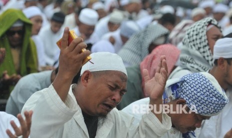 Umat muslim berdoa ditengah guyuran hujan saat mengikuti aksi damai di kawasan Monas, Jakarta, Jumat (2/12).