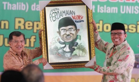 Wakil Presiden Jusuf Kalla (kiri) menerima lukisan karikatur dari Rektor Unisma, Maskuri (kanan) saat pemberian gelar Bapak Perdamaian di Universitas Islam Malang, Jawa Timur, Sabtu (31/10). 