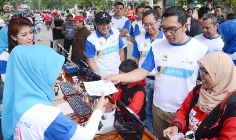 Wali Kota Bandung Ridwan Kamil (kanan) dan Dirut Bank BJB Bien Subiantoro (bertopi) bersama para pembayar PBB pada launching 'PBB Online Mobile'di Kota Bandung, Ahad (23/2).