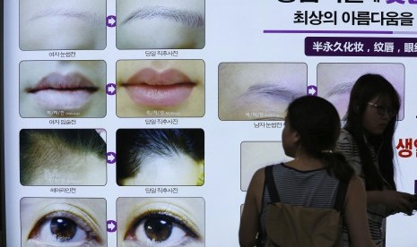 Wanita melewati papan iklan yang menawarkan jasa operasi bedah plastik untuk kecantikan di Korea.