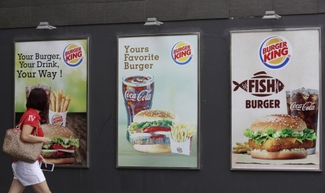 Wanita melintas papan promosi makanan burger dan kentang goreng.