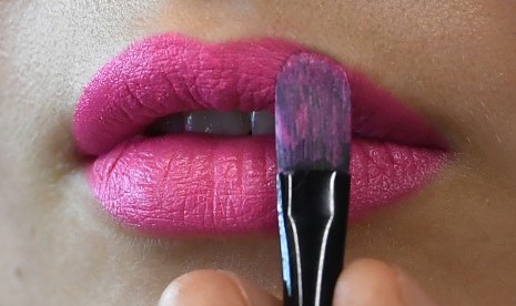 Wanita memulas bibirnya dengan lipstik.