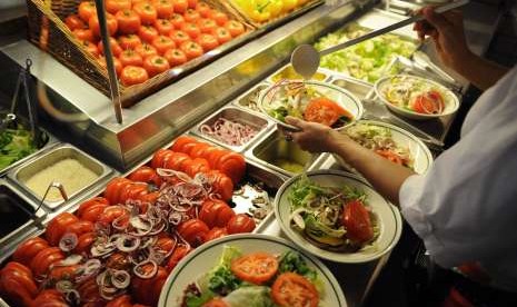 Wanita menuang saus ke atas sayuran salad.