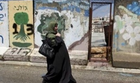     Wanita Palestina tengah berjalan di depan tembok beton yang memblokade kota Hebron, Tepi Barat. 