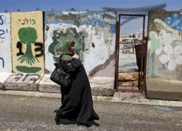 Wanita Palestina tengah berjalan di depan tembok beton yang memblokade kota Hebron, Tepi Barat. 