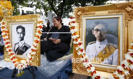 Warga Bangkok di antara dua foto raja saat  mengikuti prosesi kremasi dan penguburan jenazah mendiang Raja Bhumibol Adulyadej di Bangkok.