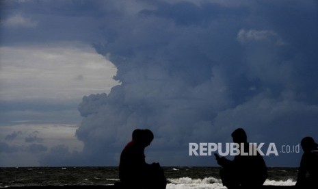 Warga beraktivitas dengan latar belakang awan panas semburan Gunung Anak Krakatau terlihat dari kawasan Carita, Pandeglang, Banten, Jumat (28/12/2018). 