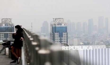 Warga beraktivitas dengan latar belakang gedung bertingkat yang terlihat samar karena polusi udara di Jakarta. Ketua DPRD DKI mengimbau warga untuk beralih ke mobil listrik terkait udara buruk.