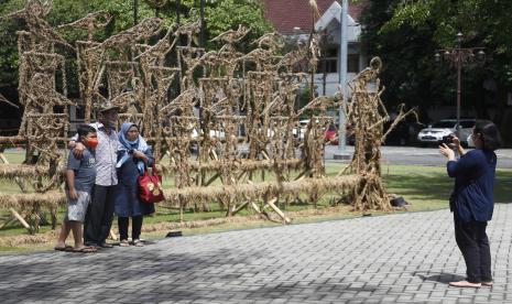 Warga berfoto dengan latar instalasi wayang berbahan jerami di halaman Balai Kota Solo, Jawa Tengah, Kamis (2/12/2021). Pemkot Solo memasang instalasi wayang jerami tersebut sebagai bentuk apresiasi terhadap karya seni perupa di Solo sekaligus dekorasi yang menarik untuk kegiatan fotografi bagi warga yang mengunjungi Balai Kota Solo.