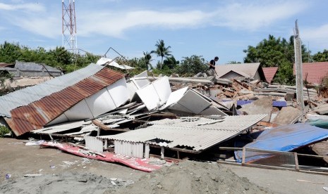 Warga berjalan di atas bangunan ruko yang runtuh akibat gempa 6.5 SR, di Meuredu, Pidie Jaya, Aceh, Rabu (7/12). 