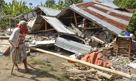 Warga berjalan di depan rumah yang roboh akibat gempa di Desa Sajang, Kecamatan Sembalun, Selong, Lombok Timur, NTB, Ahad (29/7).