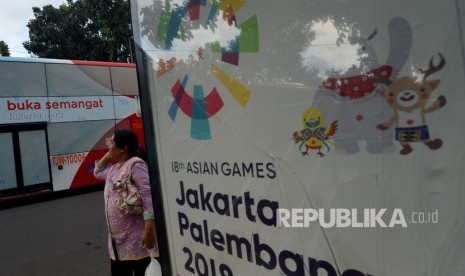 Warga berjalan di samping papan promosi Asian Games XVIII di Kawasan Jalan Merdeka Selatan, Jakarta, Jumat (20/4).