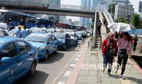 Warga berjalan kaki saat Ribuan sopir taksi dan angkutan umum lain melakukan aksi di Jakarta, Selasa (22/3).