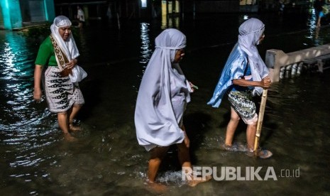 Warga berjalan menembus jalan desa yang terendam limpasan air laut ke daratan (rob). ilustrasi