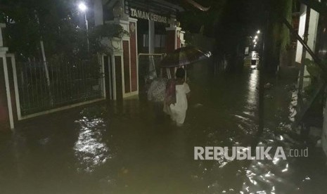 Warga berjalan menerjang genangan air di depan taman cerdas Gandekan, Solo pada Selasa (28/11).