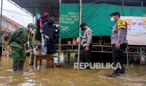 Warga berjalan turun dari panggung TPS yang terendam banjir (ILUSTRASI). BMKG memprediksi terjadinya hujan deras di Provinsi Aceh saat pencoblosan pemilihan kepala daerah pada Rabu (27/11/2024).