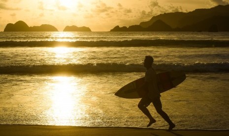 Warga berlari dengan papan selancarnya di Pantai Pulau Merah, Banyuwangi, Jawa Timur, Jumat (8/1). Pantai Pulau Merah tersebut merupakan salah satu destinasi wisata unggulan Banyuwangi.