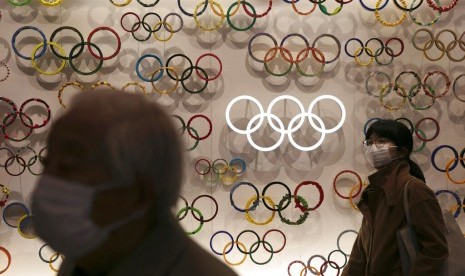 Warga bermasker melintasi Museum Olimpiade di Tokyo, Jepang. Olimpiade 2020 Tokyo ini ditunda sampai 2021 yang merupakan pertama kalinya sebuah olimpiade ditunda dalam 124 tahun sejarah olimpiade.