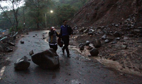 Warga berusaha melintasi material longsor yang jatuh di ruas jalan nasional Trenggalek-Ponorogo Kilometer 16, Trenggalek, Jawa Timur, Rabu (25/1).