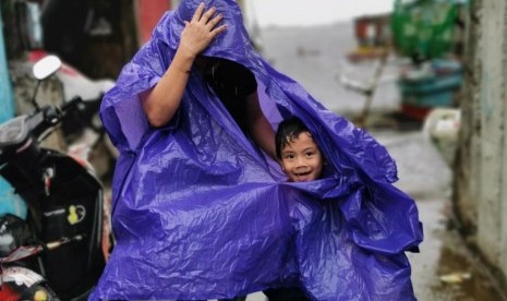 Warga di Cavite City, Filipina berjalan menggunakan mantel. Sebanyak 200 ribu orang di Filipina dievakuasi akibat topan Kammuri pada Selasa (3/12).