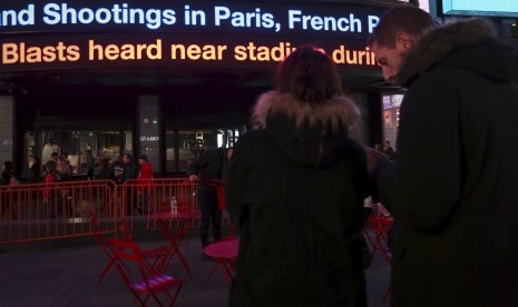 Warga di Manhattan, AS, memperhatikan berita lewat running text mengenai penembakan yang terjadi di Paris, Prancis, Jumat malam waktu setempat (13/11).