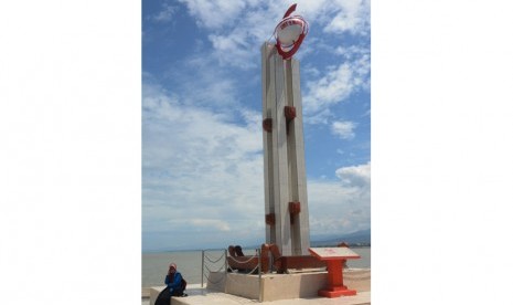 Warga duduk di dekat monumen Gerhana Matahari Total yang dibangun di bibir pantai Teluk Palu, Sulawesi Tengah, Selasa (8/3).