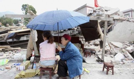 Warga duduk di samping reruntuhan rumah yang hancur akibat gempa bumi di Longmen Township, Lushan County, Ya'an, provinsi Sichuan, Cina.