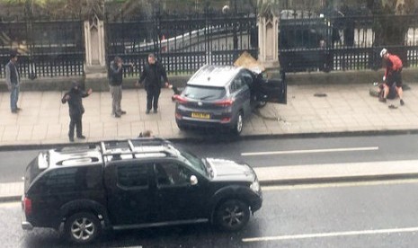 Warga Inggris berkumpul dekat sebuah mobil yang kecelakaan dan seseorang yang terbaring di tanah (kanan) di Bridge Street dekat Gedung Parlemen Inggris di London, Rabu (22/3). Terjadi serangan penusukan di dekat parlemen.