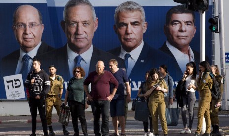 Warga Irael menunggu lampu lalu lintas menyala hijau di depan poster para pemimpin Partai Blue and White, (dari kiri ke kanan) Moshe Yaalon, Benny Gantz, Yair Lapid dan Gabi Ashkenazi, di Ramat Gan, Israel, Ahad (7/4).