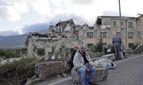 Warga Italia duduk di tepi jalan. Gedung yang hancur di Amatrice, Italia terlihat di belakangnya, Rabu, 24 Agustus 2016.